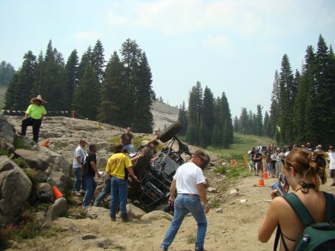 1989 Ford Bronco - An off-road vehicle has overturned on a challenging rocky course, with onlookers gathered.