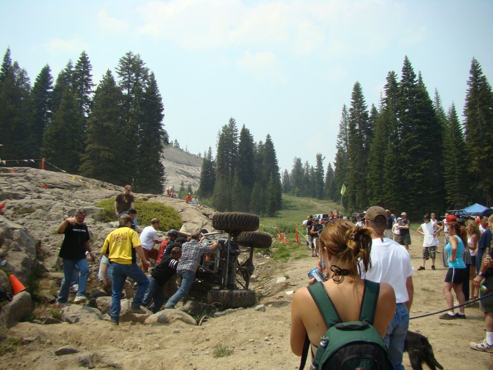 Off-road vehicle on its side with people around it on a rocky, wooded trail