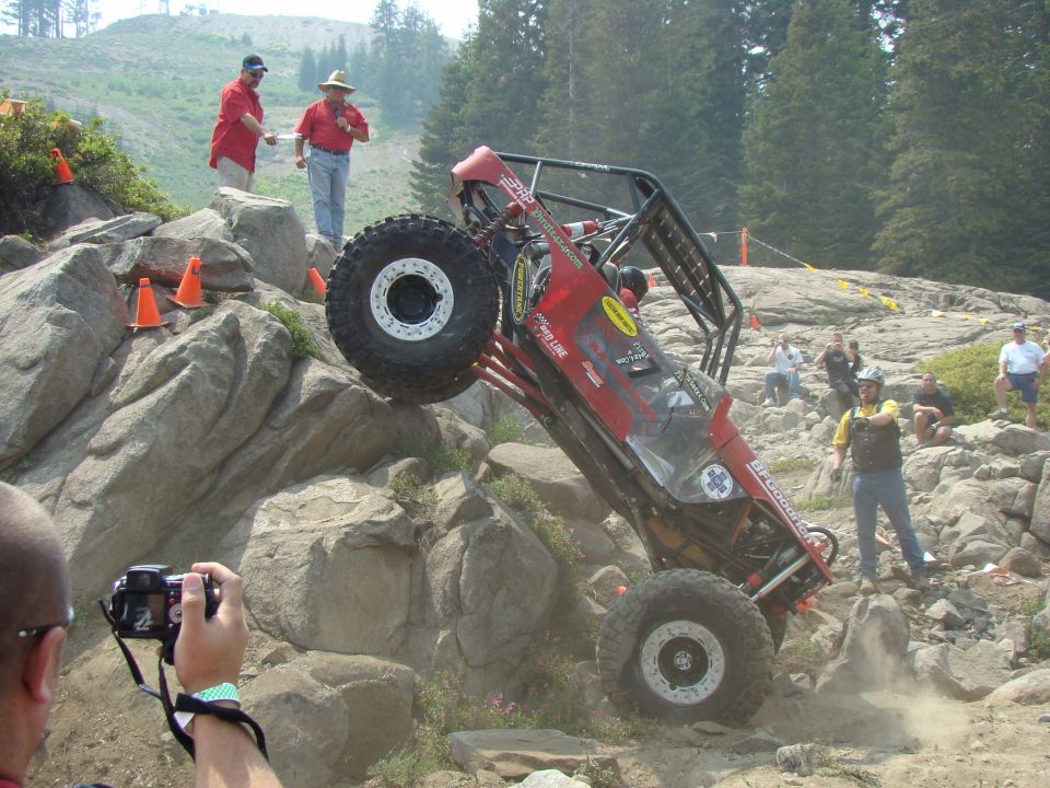 Red off-road buggy tilted on rocks, with a roll cage and large tires