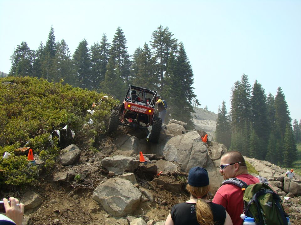 Red off-road buggy climbing rocks, with people watching