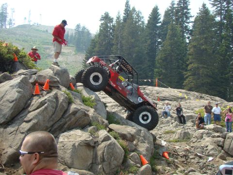 1989 Ford Bronco - A red off-road vehicle navigates a challenging rocky course with spectators watching.
