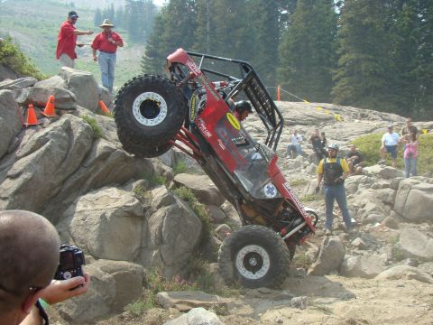 1989 Ford Bronco - A heavily modified off-road buggy navigates a challenging rocky terrain with spectators watching.