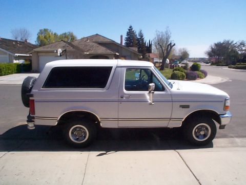 1994 Ford Bronco - A white Ford Bronco is parked on a residential street with houses and trees in the background.