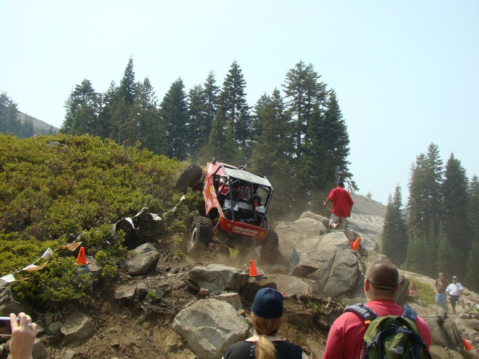 Red off-road buggy navigating a steep, rocky incline with spectators watching