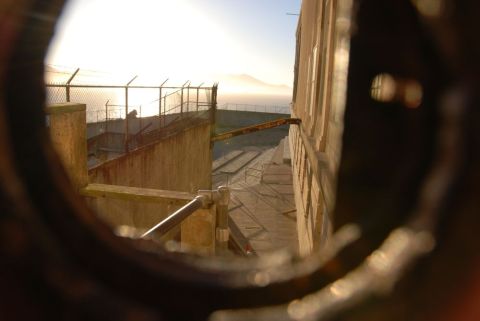 1996 Ford Bronco - A view through a circular opening shows a desolate prison yard with a fence and a distant hazy coastline.