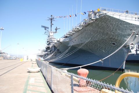 1996 Ford Bronco - A large aircraft carrier is moored at a harbor, with flags flying from its mast.