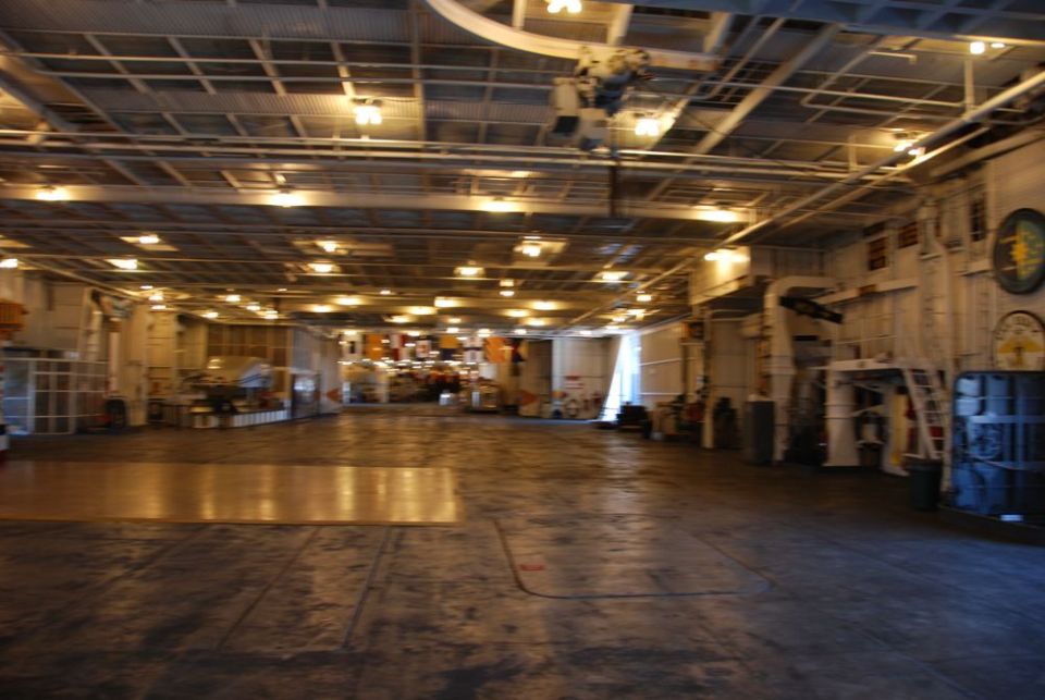 Interior of a large, empty industrial space with overhead lighting and storage units along the walls