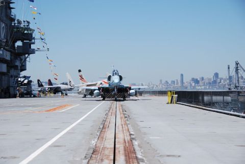 1996 Ford Bronco - Fighter jets are parked on an aircraft carrier deck, with a city skyline visible in the distance.