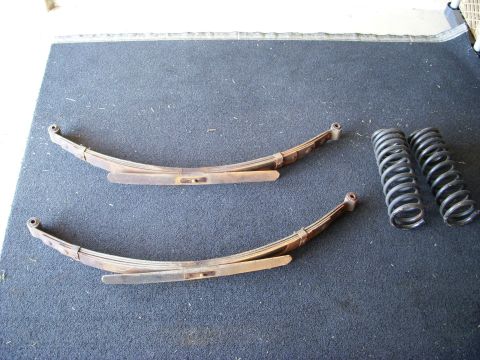 1977 Ford Bronco - Pair of leaf springs and coil springs are laid out on a dark surface.