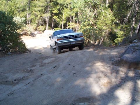 1994 Ford Bronco - A white Ford Bronco navigates a dusty, wooded trail.