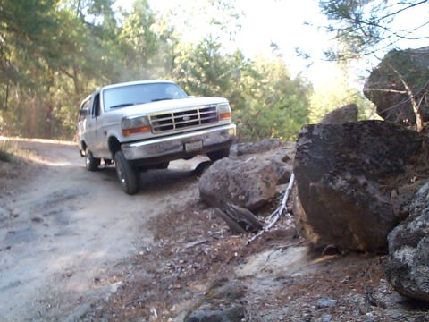 1994 Ford Bronco - A white SUV navigates a rocky, dirt path in a wooded area.