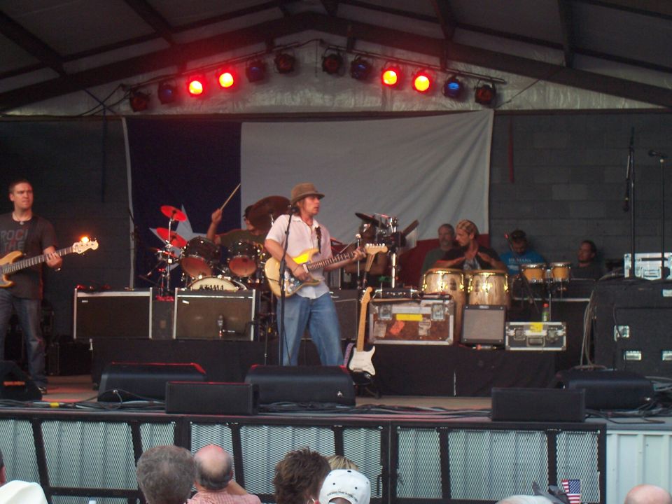 Band playing music on an outdoor stage with drums, guitars, and congas