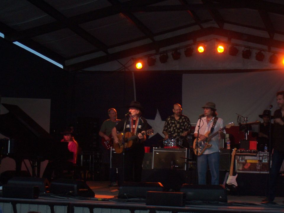 Band performing on a stage with a Texas flag backdrop. A grand piano is visible on the left