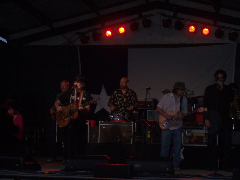 Band performing on a stage with red lights overhead and a large star on a dark backdrop