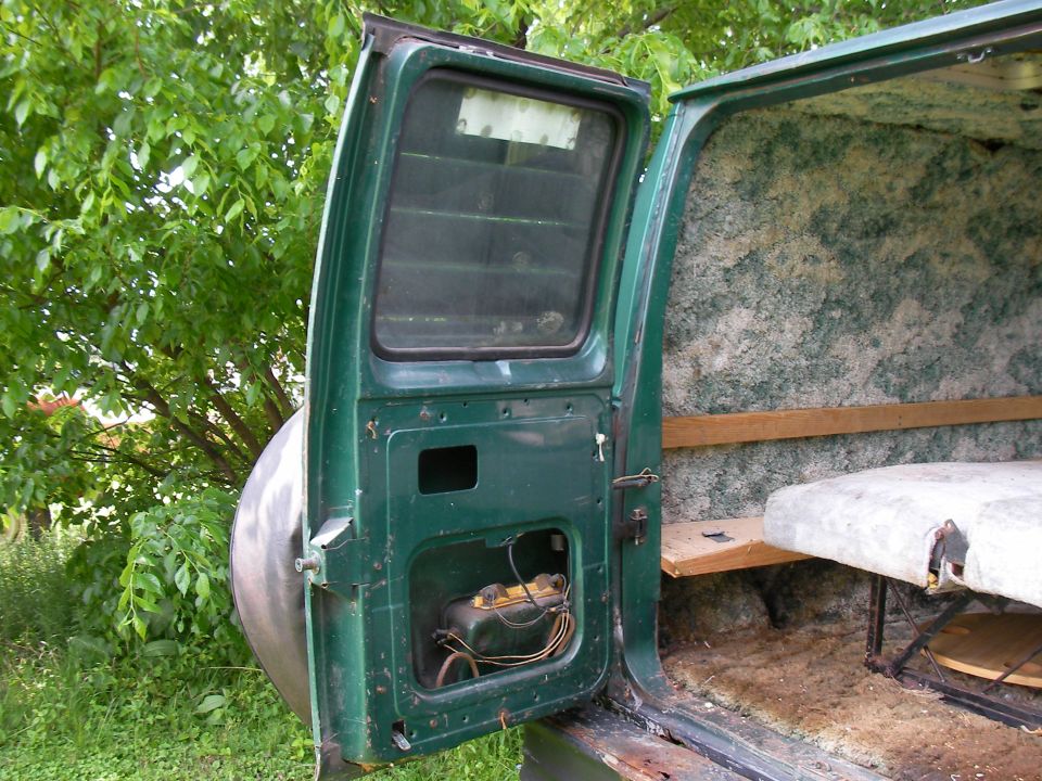 Open door of a van showing interior insulation, a wooden shelf, and a bed platform