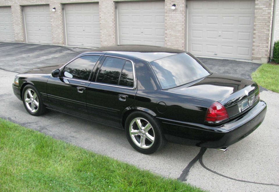 Black sedan with chrome wheels parked in front of garages.