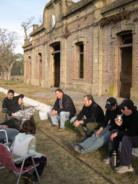 1996 Ford Explorer - Men sit on the ground and chairs near an old, abandoned brick structure under a cloudy sky.