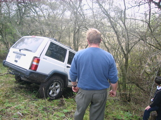 1996 Ford Explorer - A white SUV is seen stuck off-road, tilted on a grassy incline with trees surrounding it.