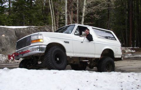 1994 Ford Bronco - White Ford Bronco with lifted suspension and large tires driving in a snowy wooded area.