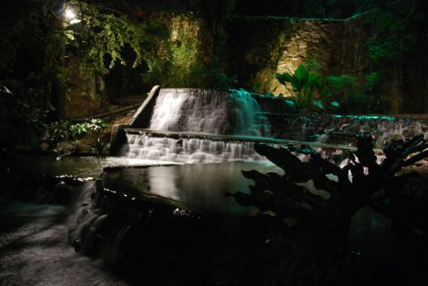 1996 Ford Bronco - A waterfall cascades down stone steps at night, surrounded by tropical plants and illuminated by soft lighting.