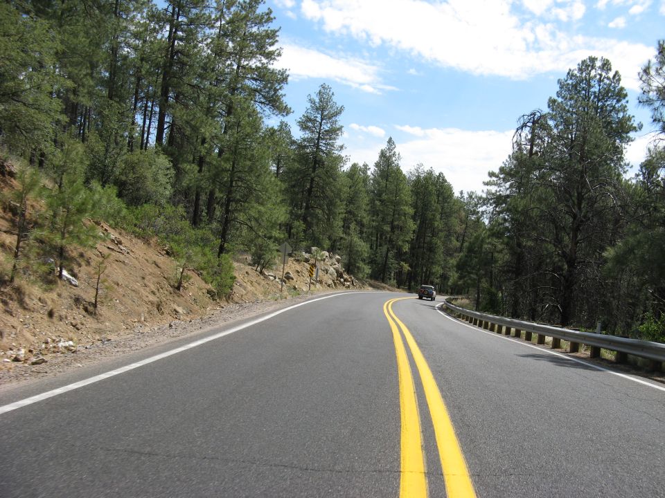 Car driving on a winding road through a forest, seen from the perspective of another vehicle