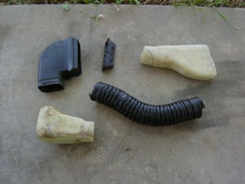 1986 Ford Bronco - A collection of automotive ducting and hoses, including a black elbow piece and a flexible corrugated tube, are displayed on a concrete sur…