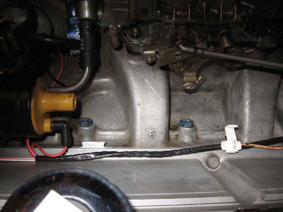 Close-up of engine intake manifold with carburetor linkage and ignition coil