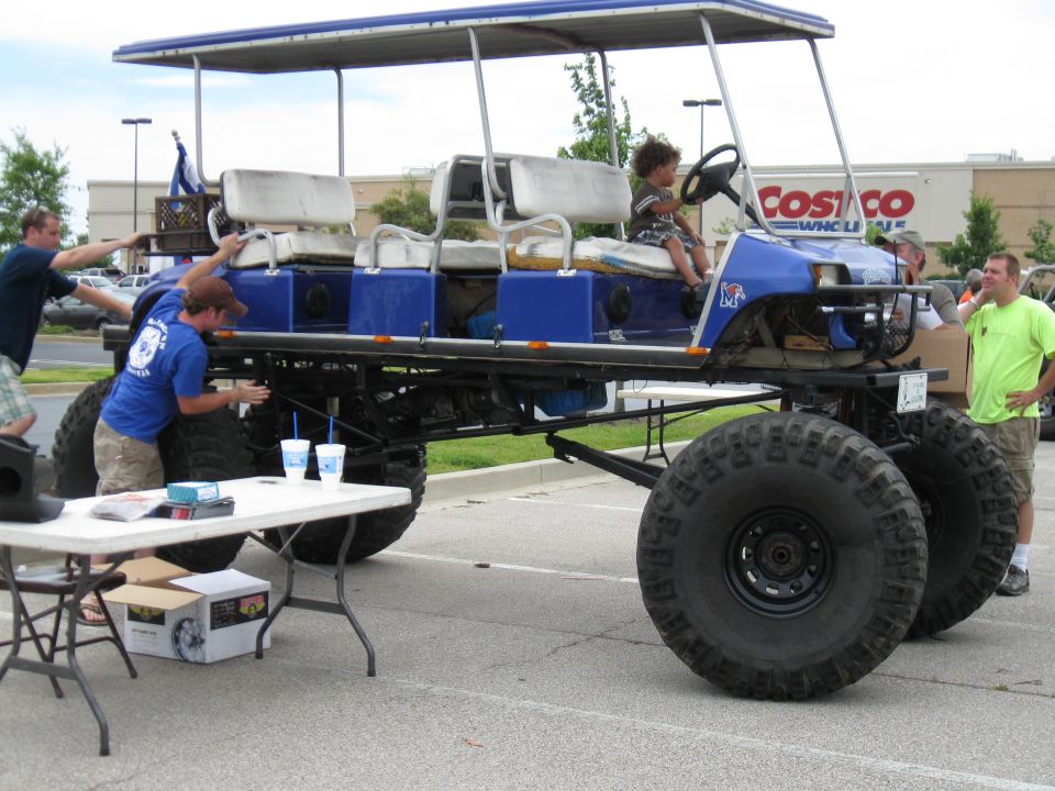 Modified golf cart with four rows of seats and oversized tires, a child is in the driver's seat