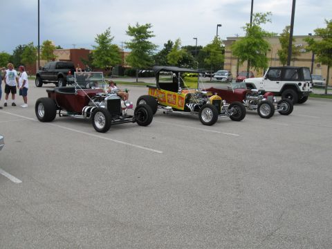 1994 Ford Bronco - A collection of custom hot rod vehicles are displayed in a parking lot under an overcast sky.
