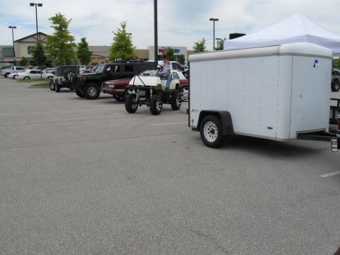1994 Ford Bronco - A modified golf cart with oversized tires is parked in a lot next to other vehicles and a trailer.