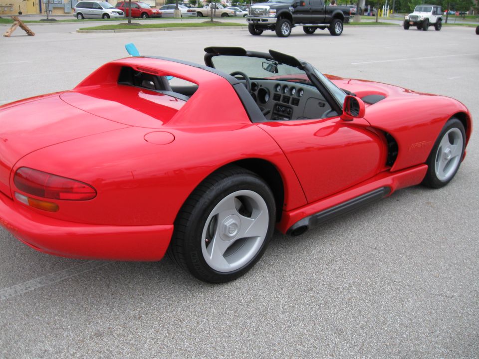 Red convertible sports car, likely a Dodge Viper, parked on asphalt. Side profile shows distinctive wheels and side exhaust