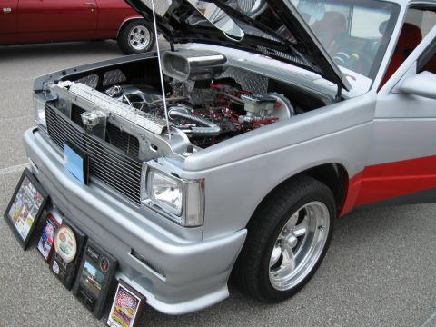 1994 Ford Bronco - A customized pickup truck is displayed with its hood open, revealing the engine, and several awards are placed on the ground in front.