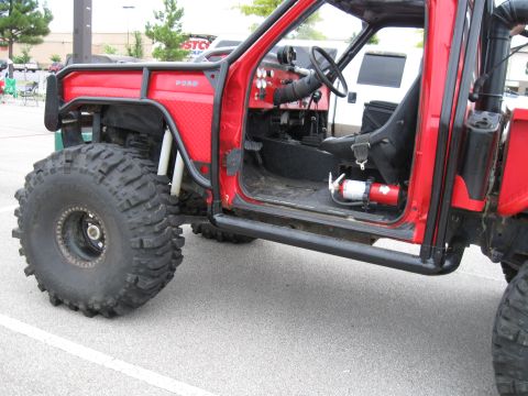 1994 Ford Bronco - This heavily modified off-road vehicle features oversized tires, a roll cage, and a visible 'FORD' badge on its fender.