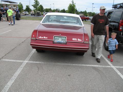 1994 Ford Bronco - Rear view of a red 1980 Chevrolet Monte Carlo parked in a lot, with a man and child walking by.