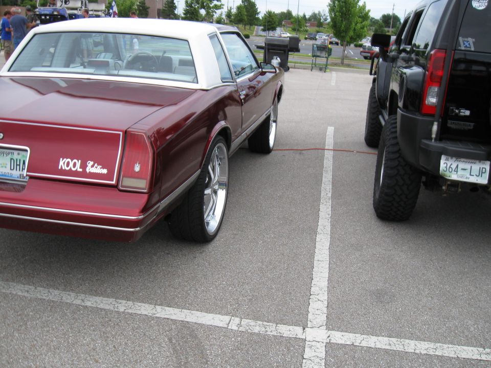 Maroon coupe with white roof and chrome rims parked next to a black SUV