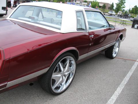 1994 Ford Bronco - A maroon coupe with a white vinyl roof and large chrome rims is parked at an outdoor event.