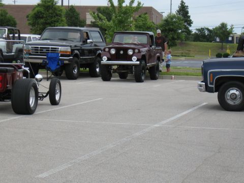 1994 Ford Bronco - Several vehicles are parked in a lot, including a 1994 Ford Bronco and a custom Jeep.