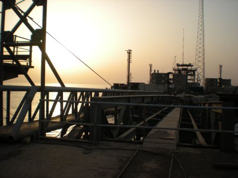 1981 Kenworth W900A - A wide view of an industrial dock area with various structures and cranes silhouetted against a hazy sunset sky.
