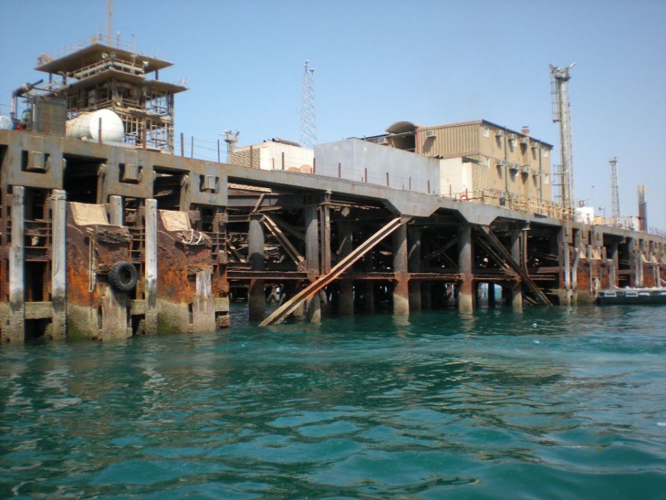 Rusted industrial pier with concrete pilings and metal framework over turquoise water
