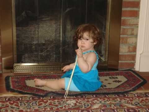 2000 Ford Crown Victoria - A young child sits on a rug in front of a fireplace, playing with sticks.