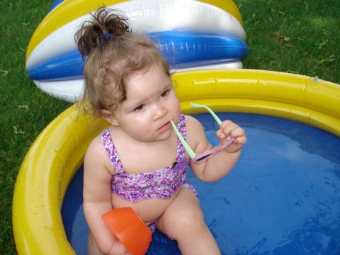 2000 Ford Crown Victoria - A baby with curly hair sits in a kiddie pool, chewing on sunglasses.