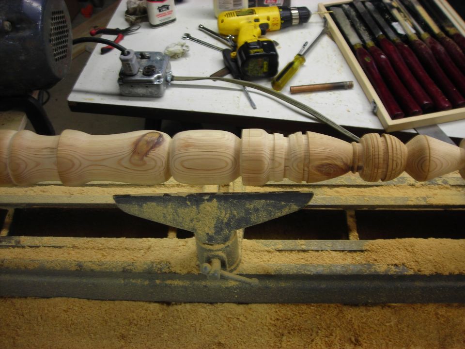 Wood spindle on a lathe with woodworking tools and drill in background