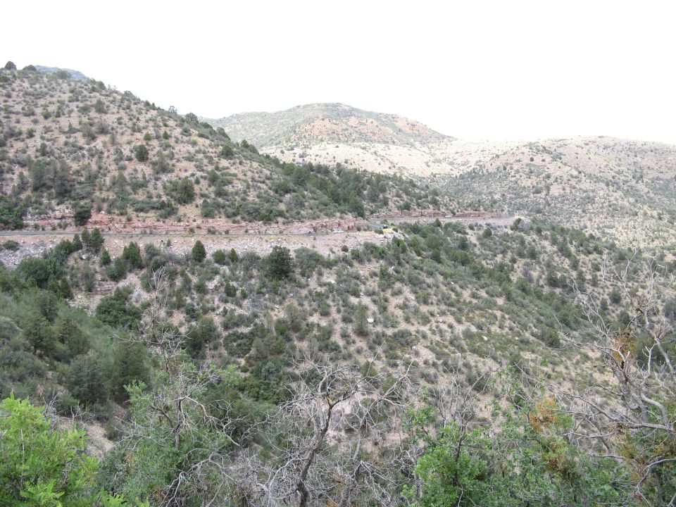 Winding road through a hilly, scrub-covered landscape under a hazy sky