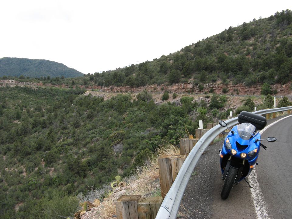 Blue motorcycle parked on a winding road with a mountainous, forested landscape