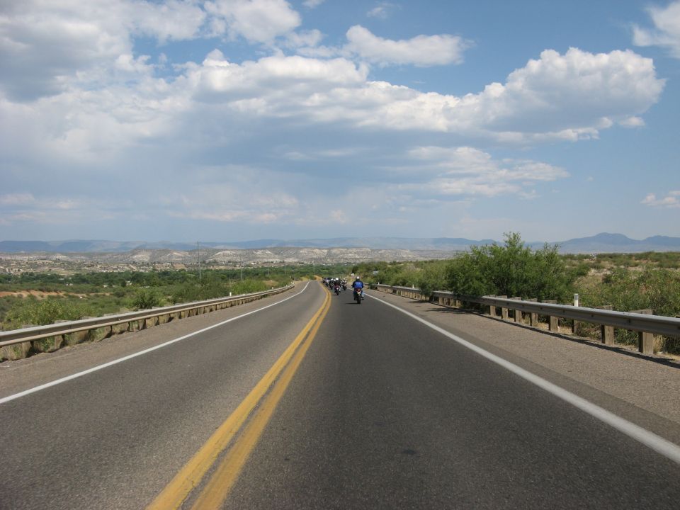 Motorcycles on a highway with a desert landscape and cloudy sky