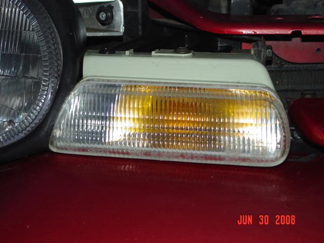 Close-up of a clear and amber turn signal assembly next to a headlight on a red vehicle