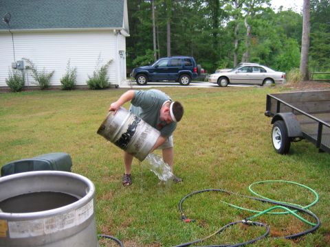 1985 Ford LTD Crown Victoria - A man pours liquid from a keg onto a grassy lawn, with two cars and a trailer nearby.