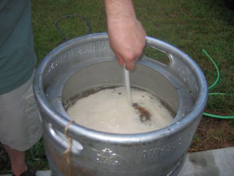 1985 Ford LTD Crown Victoria - A person stirs a foamy liquid in a large metal container, likely for brewing purposes.