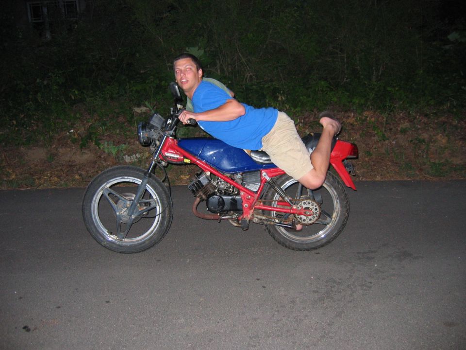 Guy straddling a red and blue motorcycle, leaning forward