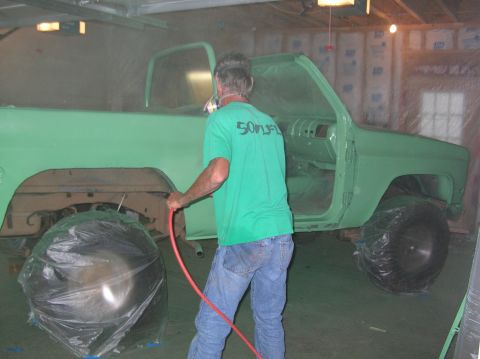 1975 Chevrolet Blazer - A person is spray painting a truck in a garage. The vehicle is covered in a light green primer.
